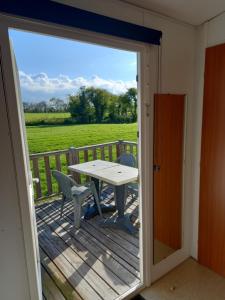 a door open to a deck with a table and chairs at mobilhomme omaha in Saint-Laurent-sur-Mer