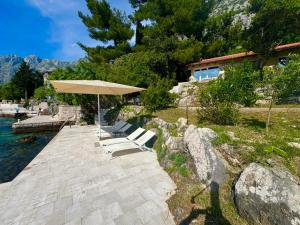 a group of benches under an umbrella next to the water at Villa Sunset, Dobrota in Dobrota