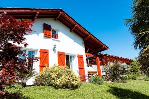 a white house with orange shuttered windows and plants at chambres hôte maison florenia in Caro
