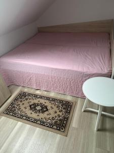 a bed with a pink sheets and a table and a rug at Kirhouse Apartment in Bohinjska Bela