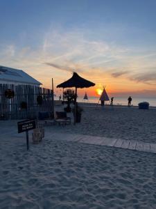 a sunset on a beach with people and an umbrella at ZeeBedStay in Noordwijk aan Zee