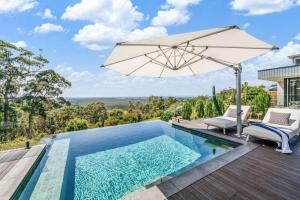 a swimming pool with an umbrella and chairs next to a house at Coolum Beach Country Retreat in Yandina Creek