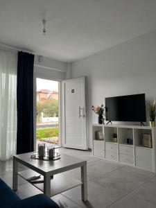 a white living room with a tv and a table at Blue Breeze Apart-Danai B in Ofrínion