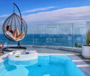 a woman sitting in a swing next to a swimming pool at Panorama Suites & Spa - Adults Only in Stómion