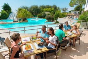 een groep mensen die aan een tafel zitten en eten bij Camping 5 étoiles - Parc aquatique - eeiaid in Pénestin
