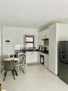 ハボローネにあるFirst Apartmentsの白いキャビネットとテーブルと椅子のあるキッチン