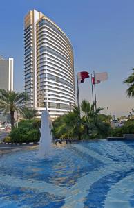 多哈White Square Curve Hotel & Suites的一座悬挂着旗帜的大楼前的喷泉