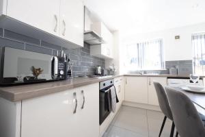 a kitchen with white cabinets and a counter with a microwave at Contemporary 3 Bedroom Home with Garden & Parking in Atherton +28 photos