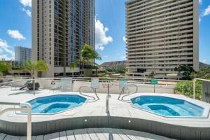 a swimming pool with two jacuzzles and two tall buildings at Steps to the Beach! Gorgeous Ocean-View Condo with Complimentary Parking (12508) in Honolulu