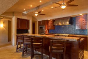 Una cocina con gabinetes de madera y una isla con taburetes de bar. en Villa Tranquilidad 7BR by Cabo Villas, en San José del Cabo