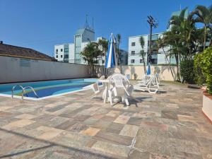 a pool with two lawn chairs and an umbrella at Apartamento Peruíbe in Peruíbe