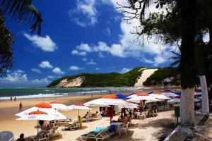 a beach with umbrellas and people sitting on the sand at 4let Verano Ponta Negra in Natal