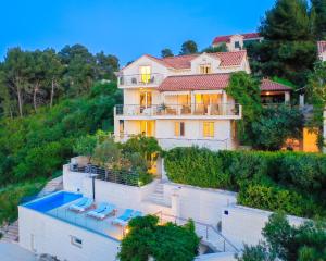 a large house with a swimming pool in front of it at VILLA PHILIPPA - luxurious five-room villa - idyllic location - first row to the sea - spectacular view of the sea bay - unforgettable sunsets - 15 minutes from Supetar ferry port - free parking - private heated pool in Sutivan