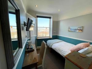 a room with a bed and a desk and two windows at Bayliss Hall Guesthouse in Weymouth