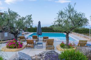 a swimming pool with chairs and an umbrella and trees at Maniatiko Village in Stoupa