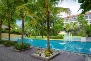a swimming pool with palm trees in front of a building at Tijili Hotel Benoa in Nusa Dua
