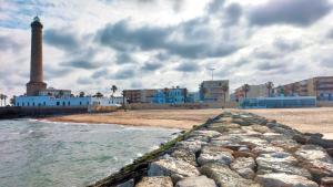 a beach with a lighthouse and buildings and the ocean at Hostal Arcos Beach Chipiona in Chipiona