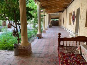 Un porche con columnas y un banco en un patio. en Nasrulla Samarqand Hotel, en Samarkand