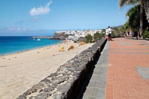 einen Bürgersteig neben einem Strand mit Leuten darauf in der Unterkunft Penthouse 3A in Morro del Jable