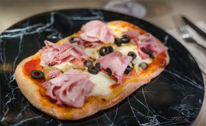una pizza con prosciutto e olive su un piatto nero di Barceló Bilbao Nervión a Bilbao