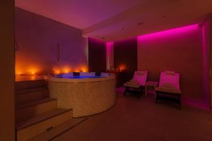 フェトヴァイアにあるHotel Galli - Wellness & Spaの浴槽と椅子2脚と紫色のライトのある部屋