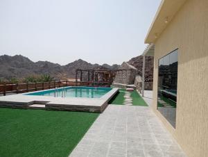 a swimming pool with green grass next to a building at Hatta Hills Farmhouse in Sharīyah
