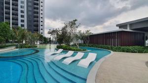 a swimming pool with white chairs in front of a building at Gamuda Cove Homestay in Banting