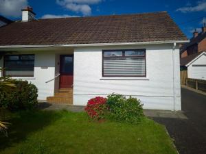 a white house with a red door and some flowers at Comfy Cottage in Ballymena