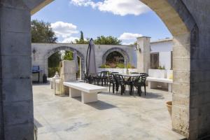 eine Außenterrasse mit Tischen, Stühlen und einem Torbogen in der Unterkunft Esclusiva tenuta salentina by Pugliadamare in San Michele Salentino
