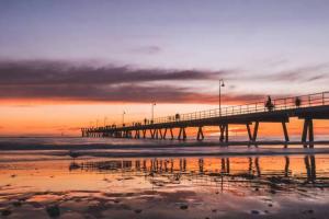 a pier with people walking on the beach at sunset at Once Upon a Tide Glenelg in Glenelg