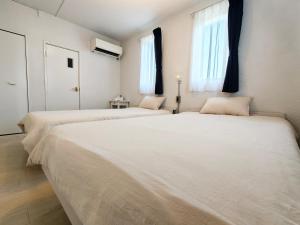 two white beds in a room with two windows at siesta YORON in Yoron