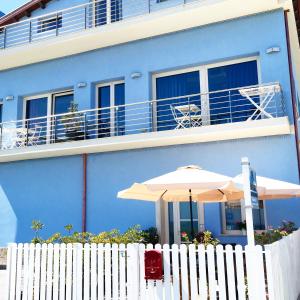 uma cerca branca com um guarda-chuva e um edifício azul em Central Rooms em Noto Marina