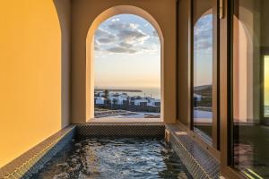 a bathtub with a view of the city seen through windows at Niabelon Suites - Private Jacuzzi Sunset View in Oia