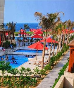 a resort swimming pool with red umbrellas and the ocean at بورتو سعيد شاليه غرفة وصالة ببورسعيد in Port Said