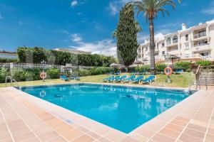 a large swimming pool with blue chairs and a building at Sunny apartment with balcony & swimming pool by REMS in Sitio de Calahonda