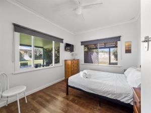 a bedroom with a bed and a desk and two windows at Margs In Mandurah- Classic Family Holiday Abode! in Dawesville