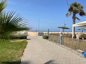 a walkway next to the beach with an umbrella at BLANCA BEACH- بلانكا بيتش سكن مشترك غرفة مزدوجة مكيفة لدى الساكن في I COLOCATION I Chambre double climatisée chez l'habitant dans une résidence pieds dans l'eau I FLAT SHARE I Air conditioned double room in a host's home within a waterfront residence in Sidi Rahal