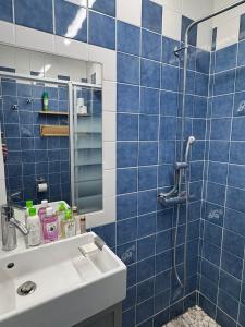 ル・ラヴァンドゥーにあるAPPARTEMENT ET SA JOLIE TERRASSE Le Lavandou Saint Clair, a deux pas de la plage de St Clair, au calme, Studio tout équipé, clim, Wifi Fibre, TV connectée, lave linge, lave vaisselle, place de parking et plus, serviettes et draps fournisの青いタイル張りのバスルーム(シンク、シャワー付)