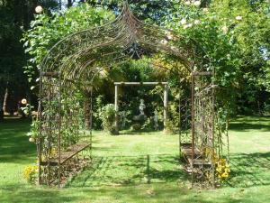 a metal arch in a garden with a statue at Kergarec gite H in Clohars-Fouesnant