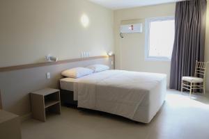 a white bedroom with a bed and a chair at Klein Ville Marquês in São Leopoldo