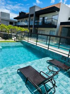 a swimming pool with two benches in front of a building at Casa da Alê in Camaçari