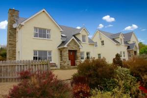 a large white house with a wooden fence at Charming Coastal Cottages by Portsalon Beach in Portsalon