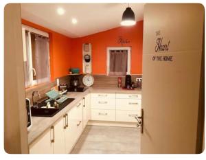 a kitchen with orange walls and white cabinets at La Maison Téranga au Bourg de Villenave in Courrejean