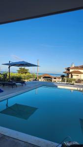 a swimming pool with two benches and an umbrella at Mediterraneo Suites with Pool & Sea View Escape in Nea Kalikratia
