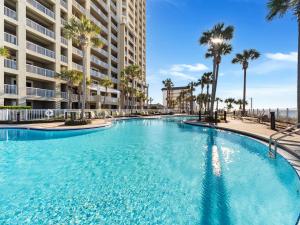 a large swimming pool with palm trees in front of a building at Grand Panama Resort - Ocean Views, Heated Pool & Tub 3 BR 3 Full BA Sleeps 10 in Panama City Beach