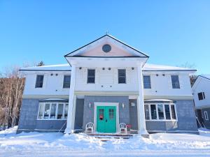 a white house with a green door in the snow at guest house White House ホワイト ハウス in Shimukappu