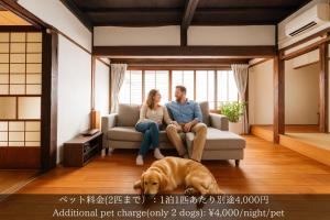 um homem e uma mulher sentados num sofá com um cão em 一棟貸切古民家,信州麹屋の宿,愛犬OK, 平日割,最大9名,Private villa em Okaya