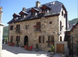 a large stone building with red chairs in front of it at CASA PIXURRI en Lanuza compuesta de 5 apartamentos turísticos en casona pirenaica, a 10 minutos de las ESTACIONES de ESQUÍ de FORMIGAL-PANTICOSA in Lanuza