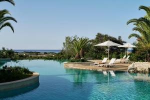 a swimming pool with chairs and umbrellas in a resort at The Westin Resort, Costa Navarino in Romanu