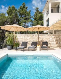 una piscina con 2 sillas y sombrillas junto a un edificio en Villa Vartal, en Ivan Dolac